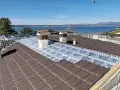 Tegole tetto moderne marroni in fase di posa su un tetto con vista lago. Sotto le tegole, una membrana isolante.