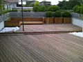 Un balcone trasformato con un pavimento in legno fai da te, circondato da piante e arredi moderni.