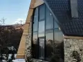 Moderna ristrutturazione casa di montagna: tetto scuro, ampie vetrate con vista sui monti, pietra e legno.