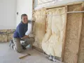 Donna con guanti installa isolamento in lana di vetro per come isolare il legno dal calore.