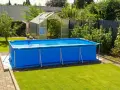 Ampia piscina blu montata in giardino, con serra sullo sfondo. Sembra una piscina senza permessi, pronta per l'estate.