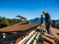 Operaio con imbracatura lavora alla costruzione tetti in legno, con vista su lago e montagne.