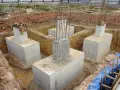 Scavi per il consolidamento fondazioni con pilastri in cemento armato e armature in vista.