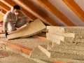 Operaio con tuta e mascherina posa pannelli isolanti, il miglior isolante termico per sottotetto calpestabile.