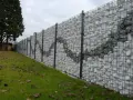 Muro di recinzione moderno con gabioni riempiti di pietre bianche e grigie, creando un motivo ondulato. Ottime idee muri di recinzione per un giardino.