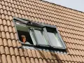 Donna guarda fuori da una finestra sul tetto, un esempio di come isolare il tetto dall'esterno per un maggiore comfort.
