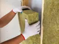 Mani guantate posizionano un pannello isolante, creando un cappotto interno o esterno per una parete.