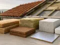 Vari materiali per la coibentazione del tetto, tra cui fibra di legno, lana di roccia e polistirene, pronti per l'installazione su una struttura in legno.
