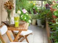 Un terrazzo fiorito e accogliente, perfetto per chi cerca idee su come abbellire un terrazzo fai da te. Tavolino in legno con bevanda rinfrescante e fiori colorati.