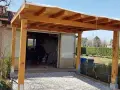 Una tettoia fai da te in legno protegge un'entrata, con un tetto in telo bianco e pilastri robusti.