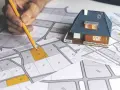 Mano con matita su mappa catastale, con modellino di casa. Pianificazione immobiliare, categoria catastale D10.
