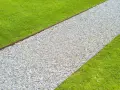 Un percorso di ghiaia bianca delimita un prato verde brillante, creando un vialetto giardino invitante.