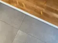 Dettaglio di piastrelle grigie posate con precisione, pronte per attaccare piastrelle al muro con silicone. Sopra, una trave di legno grezzo.