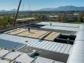 Operai installano pannelli isolanti su un tetto, riducendo il rumore. Un cantiere in corso con montagne sullo sfondo.