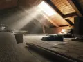Raggi di sole illuminano un sottotetto non abitabile, pieno di oggetti dimenticati e travi di legno.