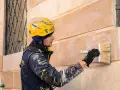 Operaio con casco giallo applica soluzione per pulire muro esterno con candeggina.