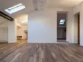 Interno moderno con pavimenti in legno e pareti in cartongesso sottotetto. Finestre sul tetto illuminano lo spazio.