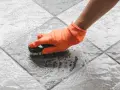 Mano con guanto arancione che strofina il pavimento del terrazzo con una spazzola, per togliere la ruggine e lo sporco.