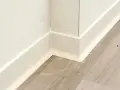 Angolo di una stanza con pavimento in laminato grigio e battiscopa bianco appena posato.