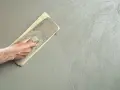 Mano che stende l'intonaco con una spatola. Dopo l'intonaco posso pitturare la parete.