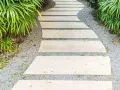 Un sentiero sinuoso con lastre di pietra e ghiaia, circondato da vegetazione lussureggiante. Idee marciapiede casa per un ingresso accogliente.