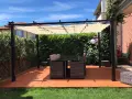 Un patio con tavolo e sedie sotto una pergola, con un **pavimento esterno economico fai da te** color terracotta.