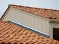 Tegole rosse su un tetto, con pannelli verticali beige e una grondaia. Le scossaline proteggono il bordo del tetto.