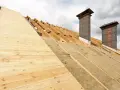 Costruzione tetto con isolamento termico: legno, lana di roccia e camini in muratura sotto un cielo nuvoloso.