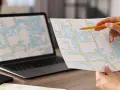 Mano con matita analizza mappa con edifici, forse per una **categoria catastale a3**. Laptop con mappa simile sullo sfondo.
