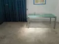 Un tavolo moderno con piano in vetro poggia su un **pavimento in cemento grezzo** dall'aspetto materico, con tende blu sullo sfondo.