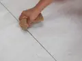 Mano che stuccare piastrelle con una spugna, rifinendo le fughe di un pavimento chiaro.
