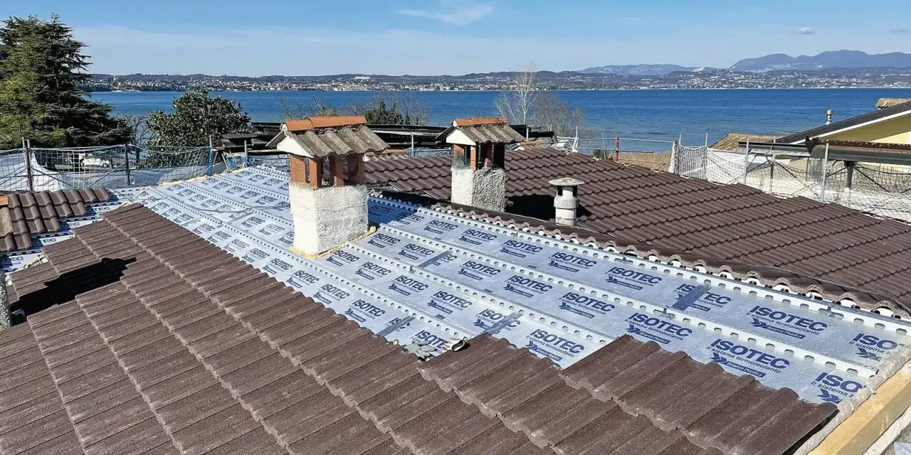 Tegole tetto moderne marroni in fase di posa su un tetto con vista lago. Sotto le tegole, una membrana isolante.