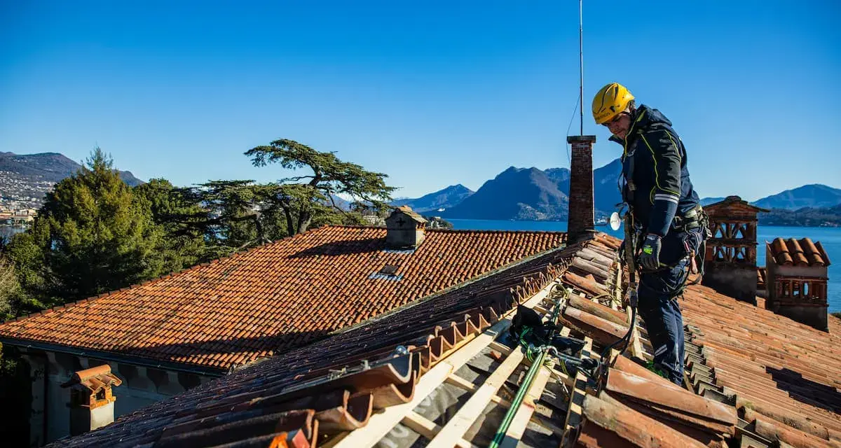 Operaio con imbracatura lavora alla costruzione tetti in legno, con vista su lago e montagne.