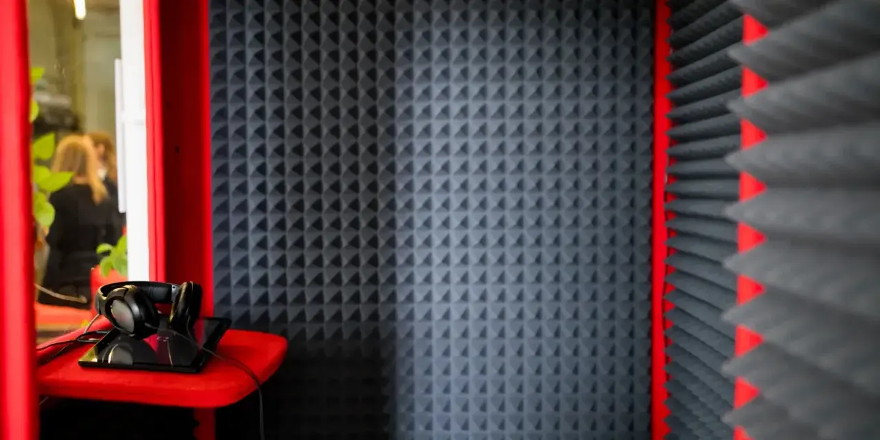 Cabina insonorizzata con pannelli fonoassorbenti, cuffie e tablet. Ideale per registrazioni audio.