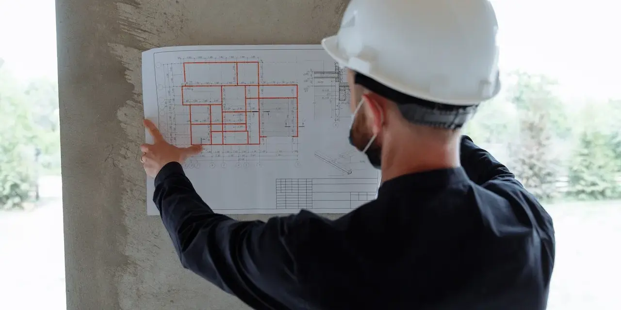 Un ingegnere con casco bianco esamina un progetto, segno che i migliori general contractor pianificano ogni dettaglio.