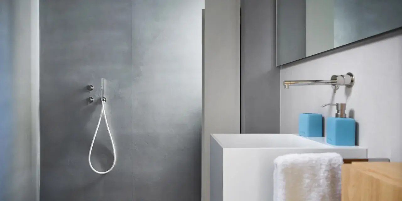 Bagno moderno con rivestimento doccia senza piastrelle effetto resina, lavabo bianco e accessori azzurri.