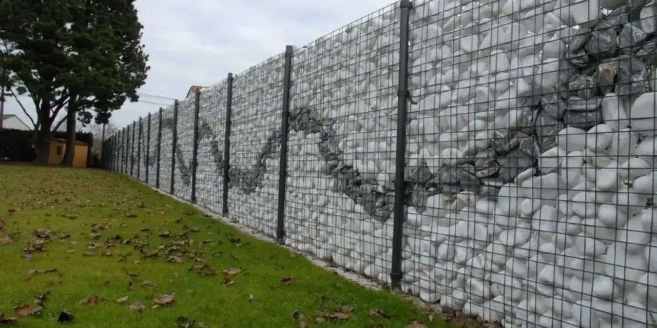 Muro di recinzione moderno con gabioni riempiti di pietre bianche e grigie, creando un motivo ondulato. Ottime idee muri di recinzione per un giardino.