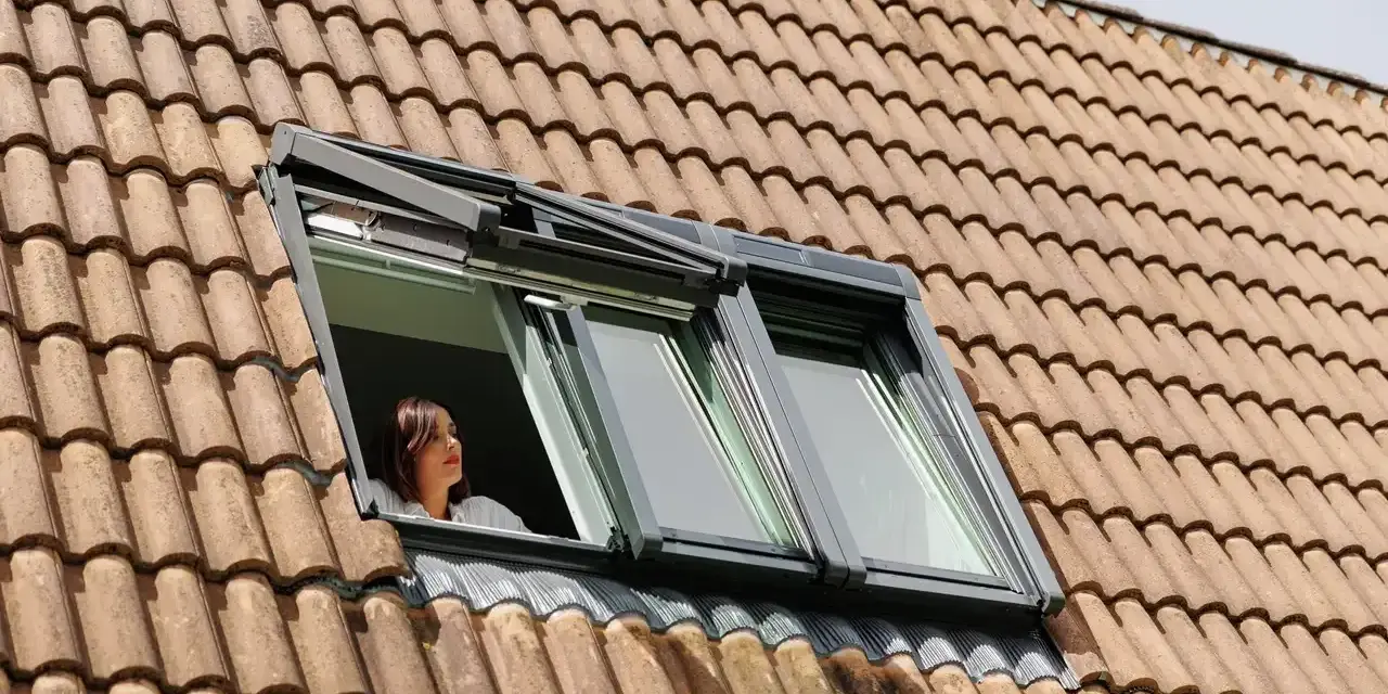 Donna guarda fuori da una finestra sul tetto, un esempio di come isolare il tetto dall'esterno per un maggiore comfort.