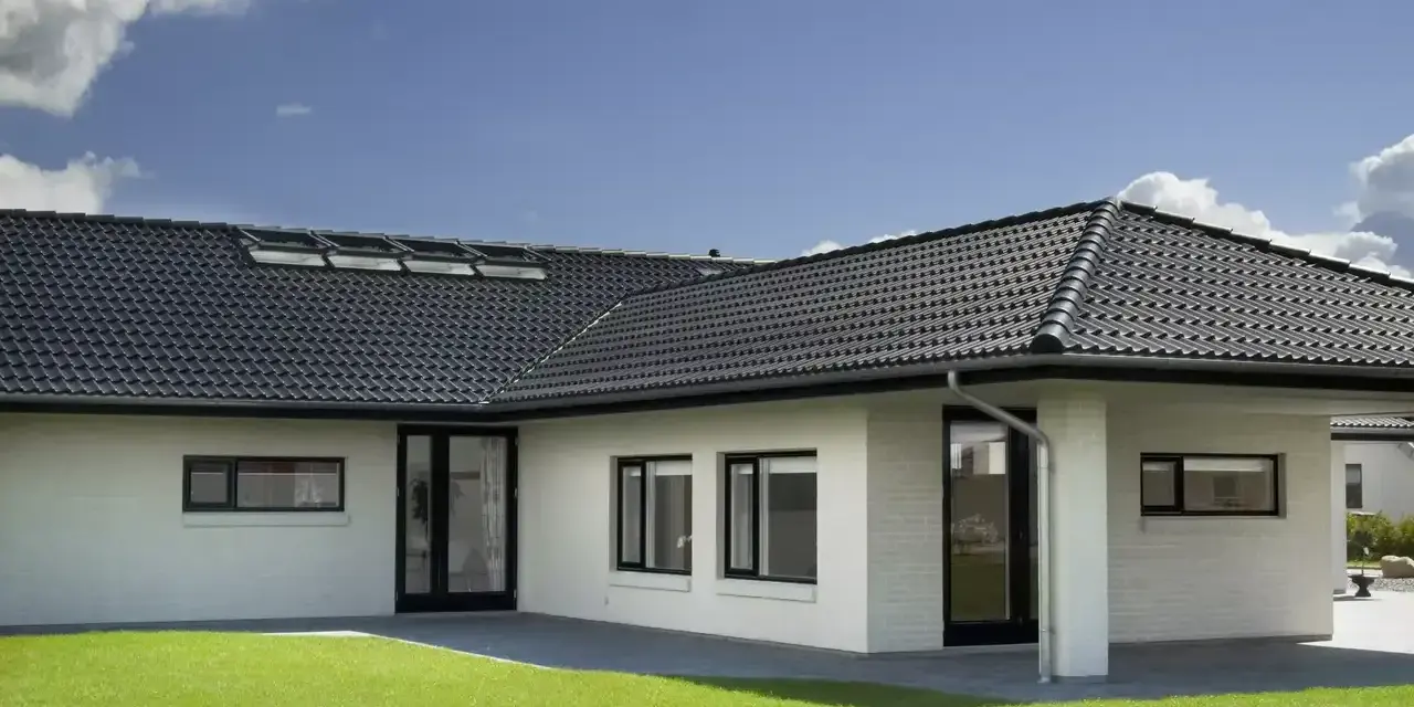 Casa moderna con tetto a padiglione scuro, finestre a tetto e prato verde.