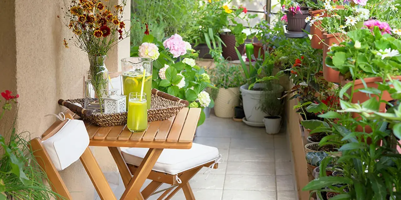 Un terrazzo fiorito e accogliente, perfetto per chi cerca idee su come abbellire un terrazzo fai da te. Tavolino in legno con bevanda rinfrescante e fiori colorati.