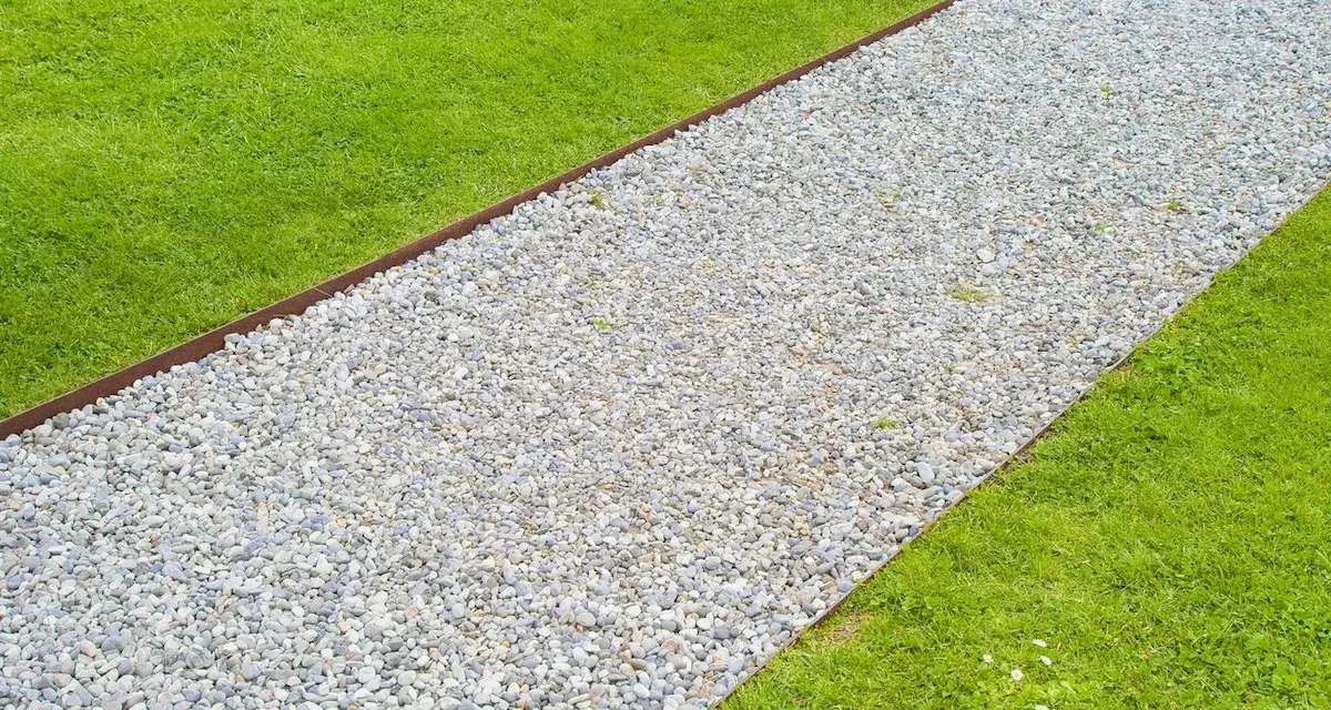 Un percorso di ghiaia bianca delimita un prato verde brillante, creando un vialetto giardino invitante.