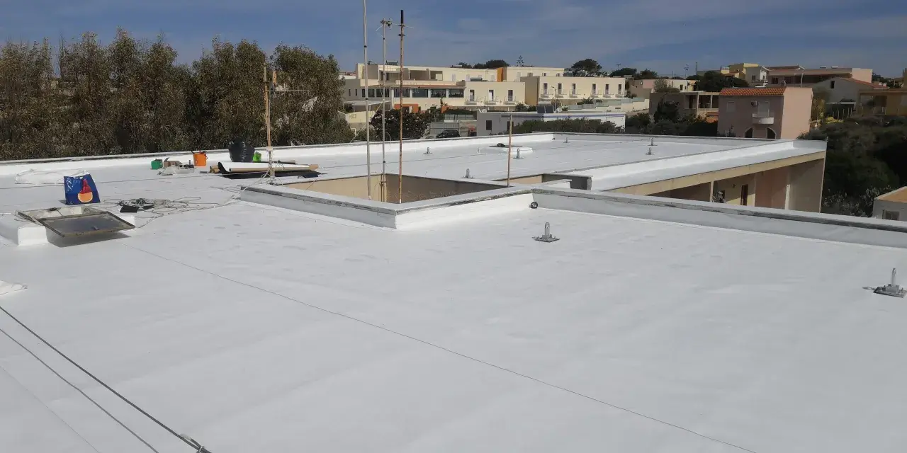 Tetto piano bianco appena impermeabilizzato senza rifarlo, con antenne e edifici sullo sfondo.