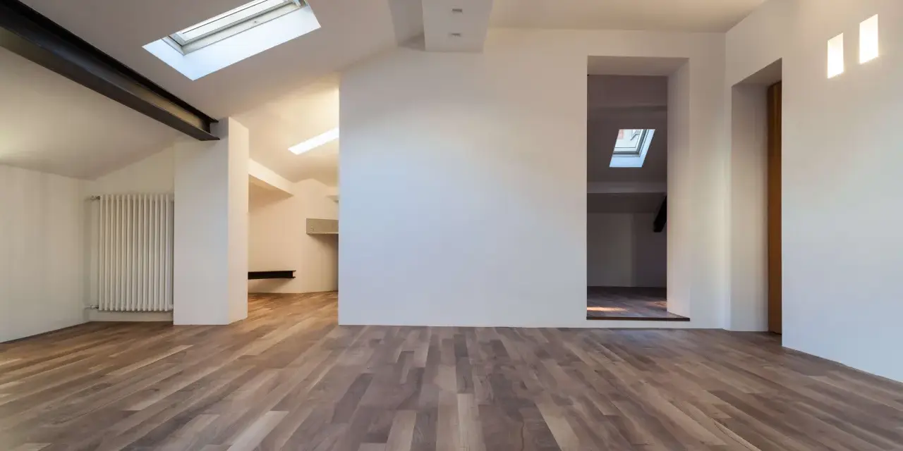 Interno moderno con pavimenti in legno e pareti in cartongesso sottotetto. Finestre sul tetto illuminano lo spazio.