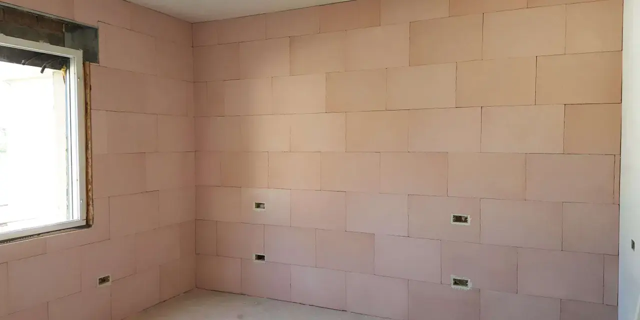 Pannelli rosa per cappotto interno con lana di roccia e cartongesso, con predisposizioni per prese elettriche e una finestra.
