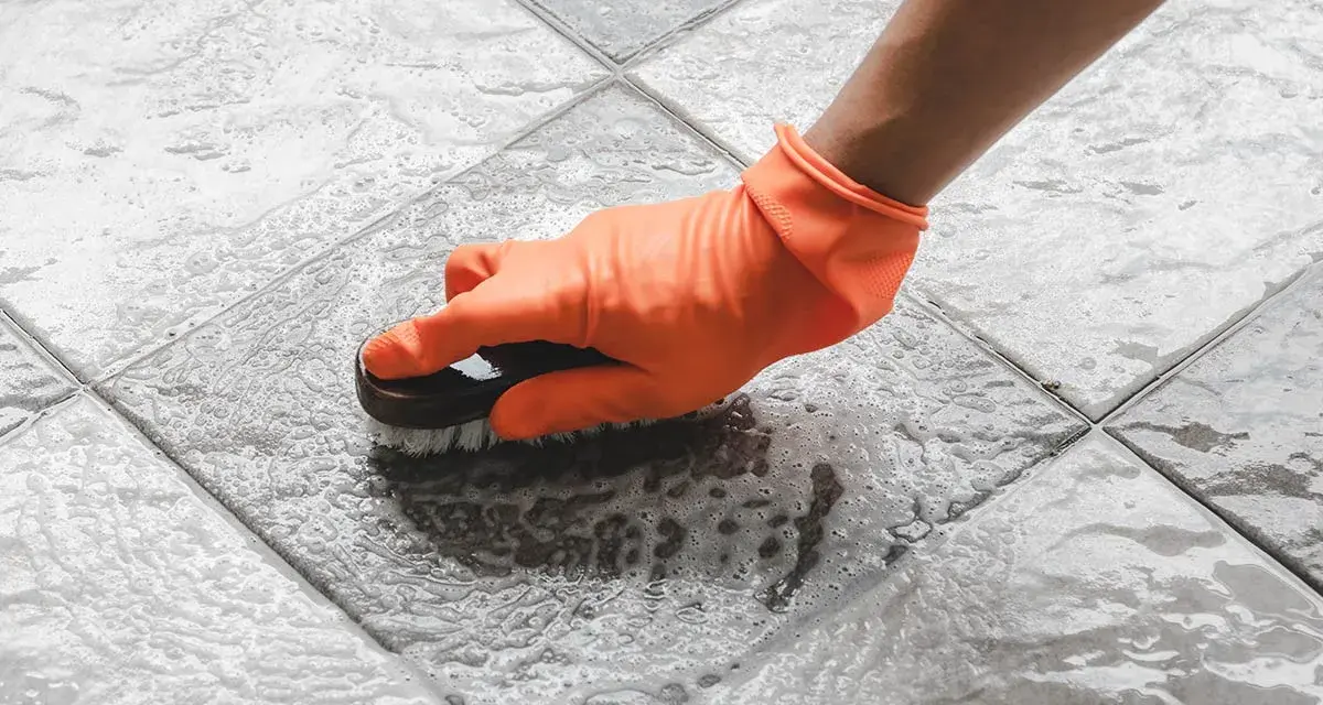 Mano con guanto arancione che strofina il pavimento del terrazzo con una spazzola, per togliere la ruggine e lo sporco.