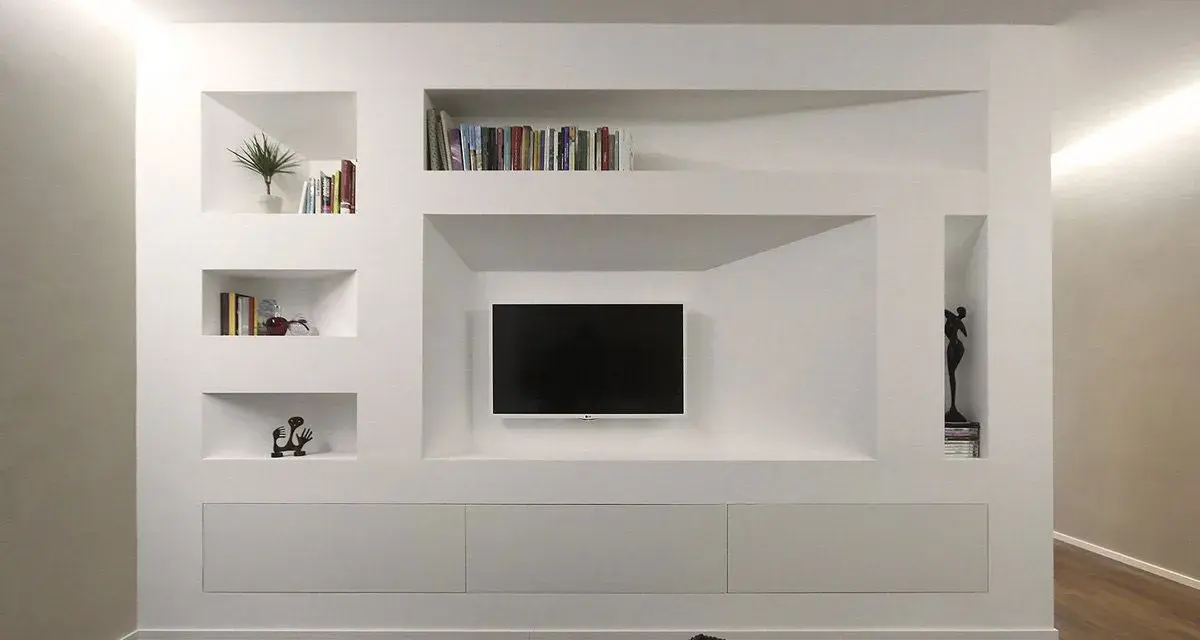 Parete attrezzata moderna con nicchie per libri e TV, realizzata in cartongesso doppia lastra, con mobili contenitori a scomparsa.