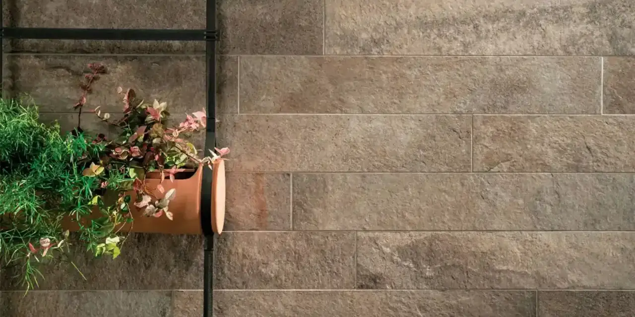 Un muro esterno rivestito con lastre effetto pietra, con un vaso di piante appeso. Ottime idee per coprire muro esterno con stile naturale.