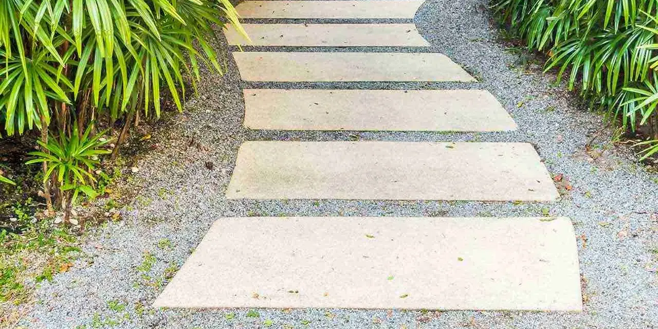 Un sentiero sinuoso con lastre di pietra e ghiaia, circondato da vegetazione lussureggiante. Idee marciapiede casa per un ingresso accogliente.