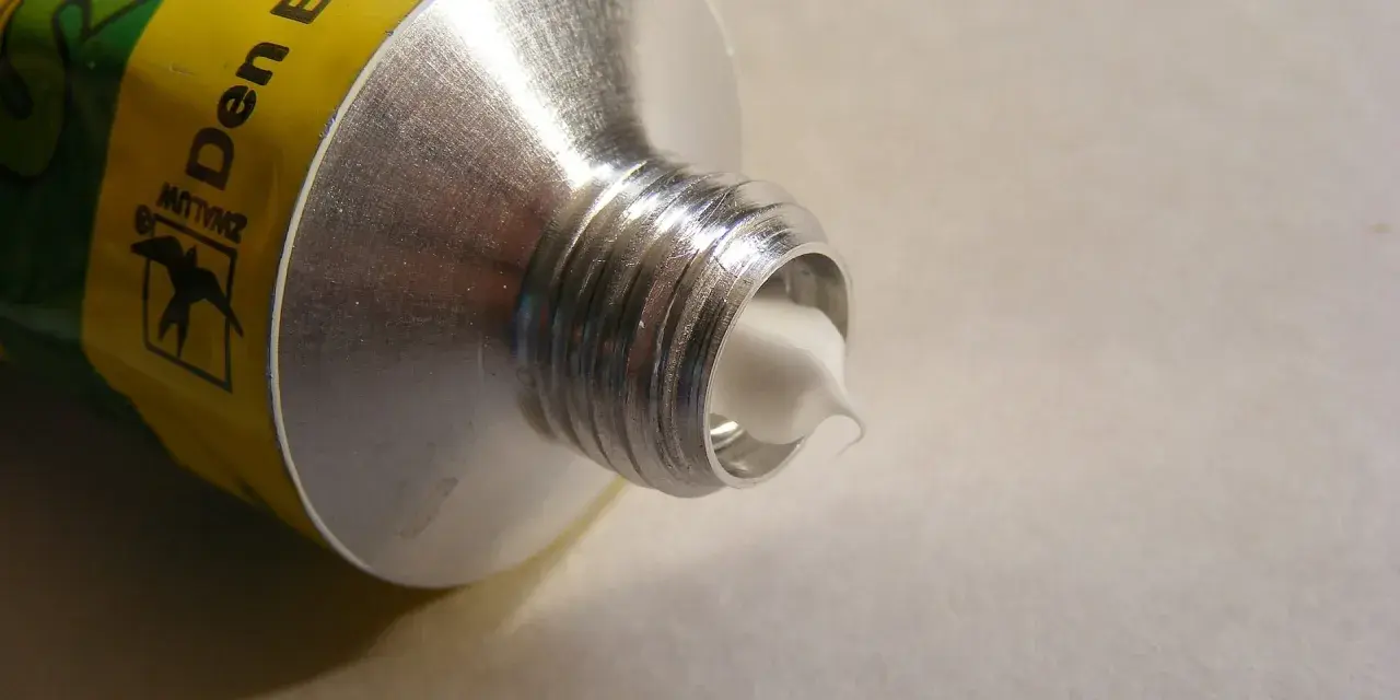Tubo di alluminio con crema bianca che fuoriesce, mostrando diversi tipi di silicone.