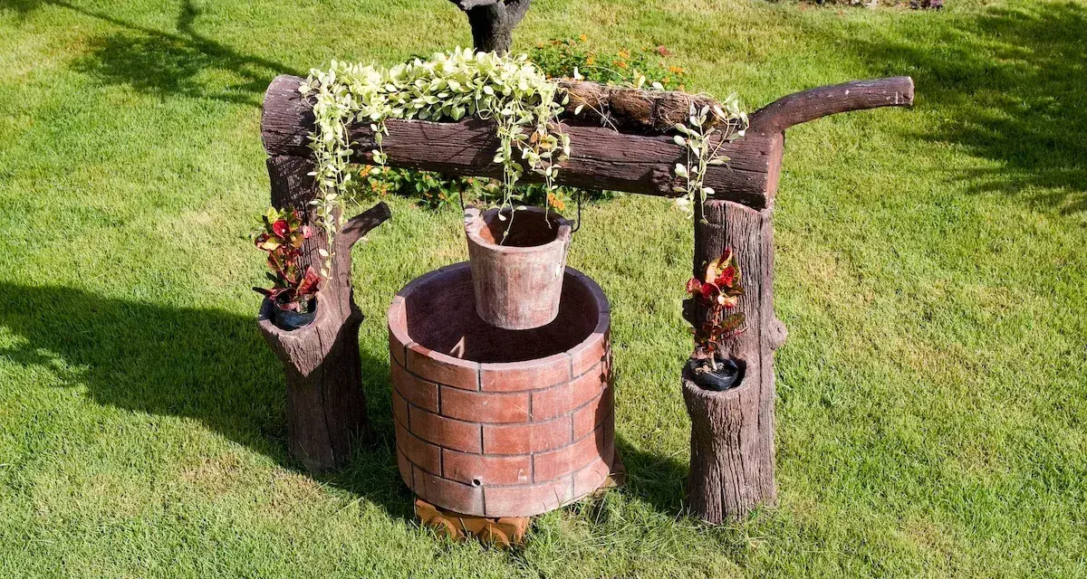 Pozzo decorativo in mattoni con secchio appeso, circondato da verde. Un'idea per capire quanto costa fare un pozzo.
